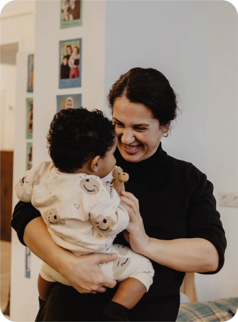 Lächelnde Mitarbeitern der FLUXi Kinderbetreuung beim spielen mit einem Kind auf ihrem Arm