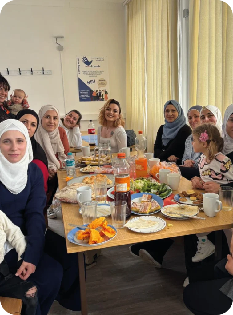 Eine Gruppe von Frauen, welche gemeinsam an einem gedeckten Tisch sitzen und lächeln. Bei einem Weltküche HILAR Event