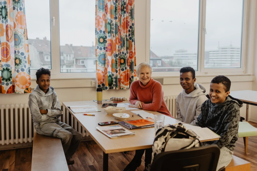 FLUX Flüchtlingshilfe Mitarbeiterin sitzend beim lernen mit 3 lächelnden Kindern