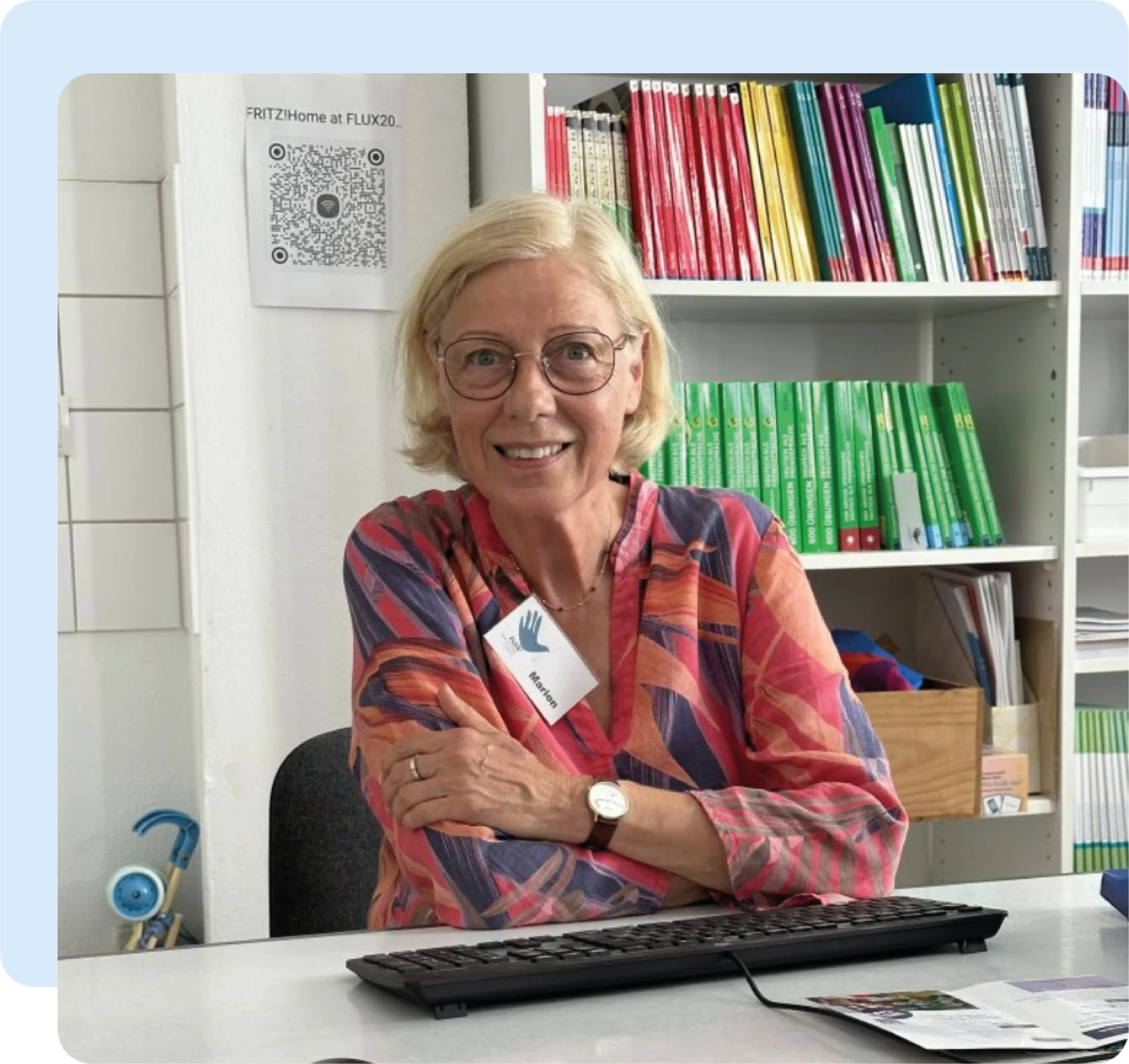 flux flüchtlingshilfe mitarbeiterin lächelnd von vorne am schreibtisch sitzend.